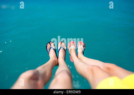 Paares Beine in Pantoffeln auf dem Meer Hintergrund Stockfoto