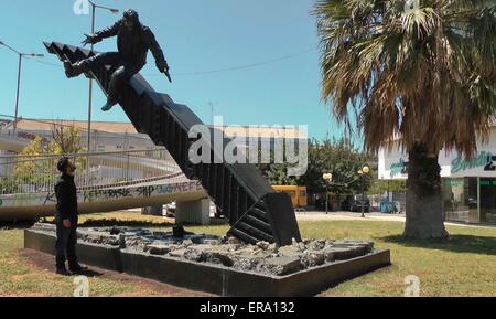 Athen. 14. Mai 2015. Foto aufgenommen am 14. Mai 2015 zeigt 22 Jahre alten griechischen Autodidakt Tasos Nyfadopoulos durch seine Skulptur "Krise" in Athen, die Hauptstadt von Griechenland stehen. Neben Vouliagmeni Avenue gelegen, nur wenige Kilometer vom Zentrum von Athen, die eindrucksvolle Skulptur, etwa 7 Meter lang und 4 Meter hoch, ist eine riesige Börsenindex, die auf dem Boden zermalmt und brach entzwei. Auf der Spitze ist ein Mann, wie der Index bricht zusammen zu fallen. © Athanasia Batziou/Xinhua/Alamy Live-Nachrichten Stockfoto