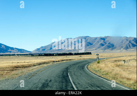 Straße führt über flache Tal zu Bergen, in der Nähe von Omarama, McKenzie Land, South Canterbury, Südinsel, Neuseeland Stockfoto