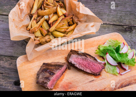 Mittlere seltene gegrillte Top Rumpsteak mit grünem Pfeffer und Thymian gewürzt serviert auf einem Holzbrett mit gebraten Rosmarinkartoffeln Stockfoto