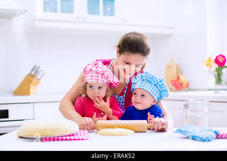 Kinder und Mutter backen. Zwei Kinder und Eltern kochen. Kleine Mädchen und Baby Boy Kochen und Backen in einer weißen Küche Stockfoto