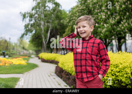 kleiner Junge im roten Hemd am Handy im freien sprechen. Junge lächelt Stockfoto