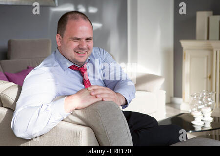 Mann in Hemd und Krawatte sitzt auf der Couch und lächelt Stockfoto