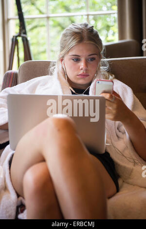 Ein blonder Teenager spielt mit ihren Laptop-Computer und iphone Stockfoto