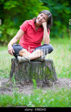ältere Frau saß auf einem Baumstumpf und lächelt Stockfoto