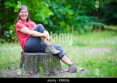 ältere Frau saß auf einem Baumstumpf und lächelt Stockfoto