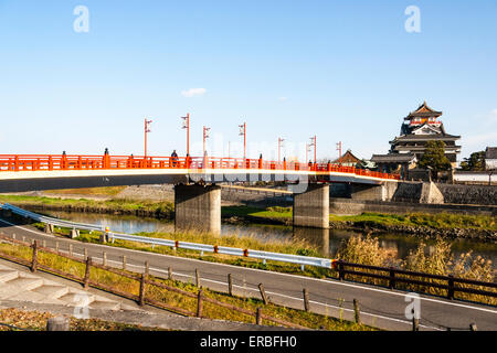 Japan, Nagoya. Betonrekonstruktion der Holzbrücke mit Melionengeländern und Lampen, die zur Burg Kiyosu mit blauem Himmelshintergrund führt. Stockfoto