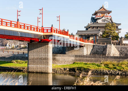 Japan, Nagoya. Betonrekonstruktion der Holzbrücke mit Melionengeländern und Lampen, die zur Burg Kiyosu mit blauem Himmelshintergrund führt. Stockfoto