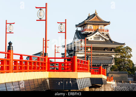 Japan, Nagoya. Betonrekonstruktion der Holzbrücke mit Melionengeländern und Lampen, die zur Burg Kiyosu mit blauem Himmelshintergrund führt. Stockfoto