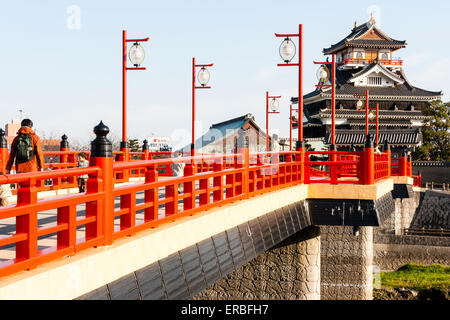 Japan, Nagoya. Betonrekonstruktion der Holzbrücke mit Melionengeländern und Lampen, die zur Burg Kiyosu mit blauem Himmelshintergrund führt. Stockfoto