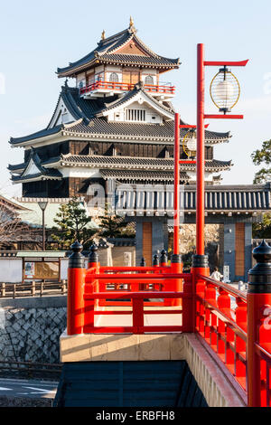 Japan, Nagoya. Betonrekonstruktion der Holzbrücke mit Melionengeländern und Lampen, die zur Burg Kiyosu mit blauem Himmelshintergrund führt. Stockfoto