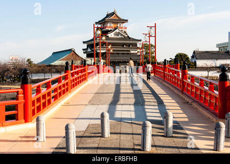 Japan, Nagoya. Betonrekonstruktion der Holzbrücke mit Melionengeländern und Lampen, die zur Burg Kiyosu mit blauem Himmelshintergrund führt. Stockfoto