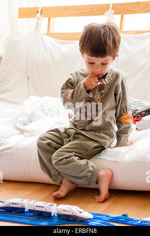 Kaukasisches Kind, Junge, 3-4 Jahre alt, sitzen drinnen zu Hause Blick auf die blaue Spur Tomy Zug Layout, mit einem rätselhaften Ausdruck. Stockfoto