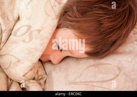 Gesicht des Kleinkindes, Jungen, 3-4 Jahre alt, braune Haare. Im Bett kuschelte sich die Bettdecke teilweise über dem Gesicht, Augen geschlossen, schlafend. Von oben betrachtet. Stockfoto