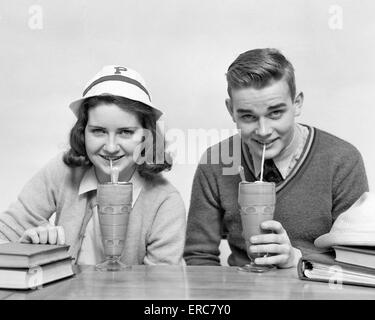 1940ER JAHRE TEENAGER-JUNGEN UND MÄDCHEN TRINKEN MILCHSHAKES ZUSAMMEN BLICK IN DIE KAMERA Stockfoto