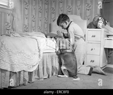 1950ER JAHRE JUNGE & HUND BETEN AM KRANKENBETT Stockfoto