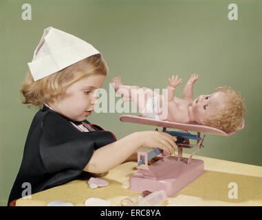 1960ER JAHRE MÄDCHEN GEKLEIDET IN KRANKENSCHWESTER KOSTÜM BELASTEN IHRE PUPPE SPIELZEUG BABYWAAGE Stockfoto