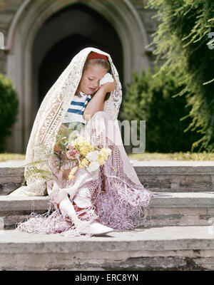 1960ER JAHRE MÄDCHEN VERKLEIDET ALS BRAUT SITZEN AUF KIRCHLICHE WEINEN VERLASSENE STUFEN Stockfoto