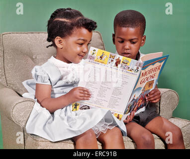 1960ER JAHREN AFRIKANISCHE AMERIKANISCHE JUNGEN UND MÄDCHEN SITZEN IM SESSEL LESEBUCH VON MUTTER GANS REIME Stockfoto