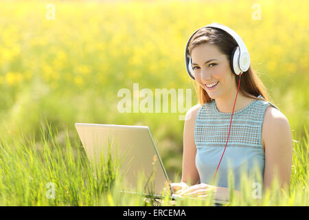 Frau arbeitet mit einem Laptop und Kopfhörer in einem Feld Blick in die Kamera Stockfoto