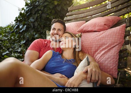 Porträt von glücklich und friedlich junges Paar auf der Hängematte im Garten entspannen. Mann mit Frau wegsehen lächelnd. Stockfoto