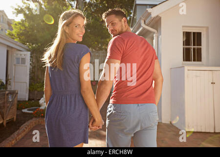 Aufnahme des jungen Paares im Garten an einem sonnigen Tag. Sie gehen zu ihrem Haus hand in hand mit Blick auf ihre Umhängeta Stockfoto