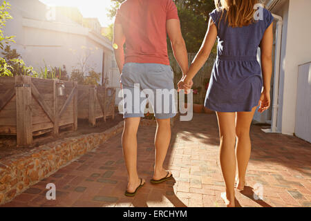 Aufnahme des jungen Paares zu Fuß in Richtung ihres Hauses zusammen beschnitten. Rückansicht des Paares im Spaziergang auf einem hellen sonnigen Hinterhof Stockfoto