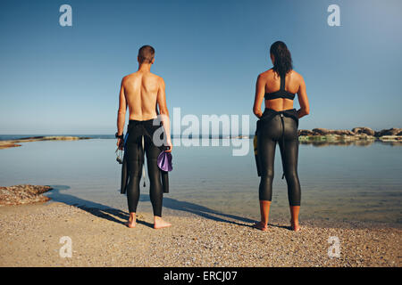 Rückansicht der jungen Athleten stehen auf See Triathlon vorbereiten. Mann und Frau, die Vorbereitung auf ein Rennen einen Neoprenanzug tragen. Stockfoto