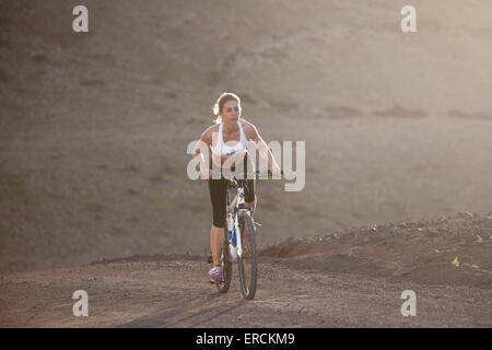 Ein blondes Mädchen reitet ihr Fahrrad bergauf auf einer felsigen Stelle auf Fuerteventura, Kanarische Inseln Stockfoto