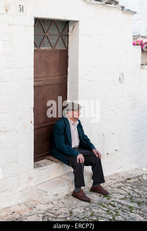 Alter Mann sitzt und Relaxes vor Trullo House, Alberobello, Apulien, Italien Stockfoto