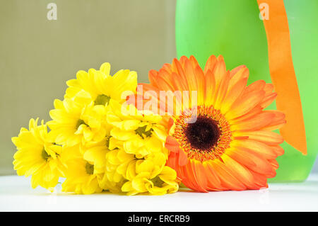 Die orange Gerbera und gelbe Daisy in der Nähe ein grünes Glasvase Stockfoto