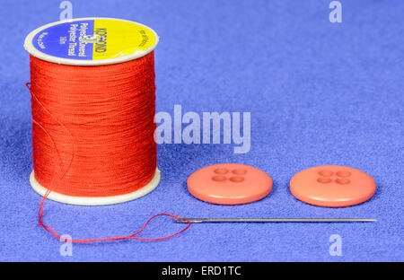 Nahaufnahme einer Spule aus roter Baumwolle mit roten Tasten und ein Gewinde Nähnadel. Stockfoto