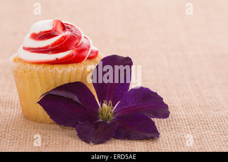 Cupcake mit einer Clematis Blume auf Sackleinen Hintergrund - ein einfaches romantisches Geschenk Stockfoto