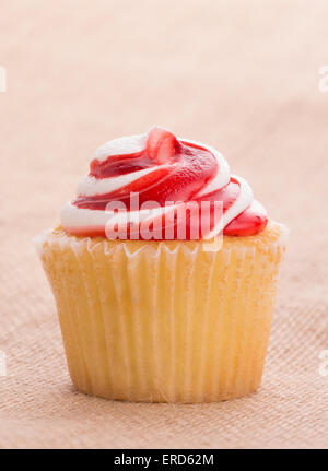 Köstliche rote und weiße swirly Top Erdbeer Cupcake auf einfache Sackleinen Hintergrund Stockfoto