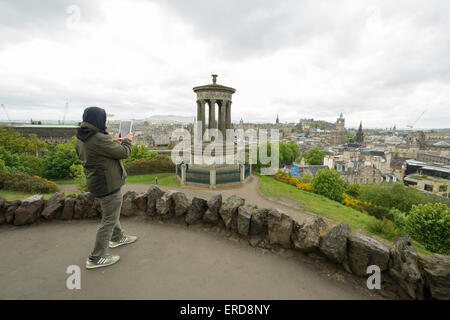 Mann, der ein Foto auf ein Ipad von Dugald Stewart Monument und Aussicht auf Edinburgh vom Calton Hill an einem grauen, bewölkten Tag Stockfoto