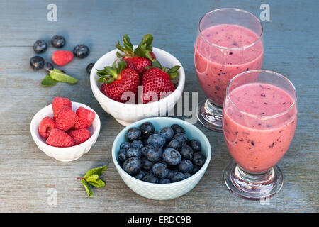 Frischen Beeren-Smoothies in zwei Gläser auf rustikalen hölzernen Hintergrund und Schalen mit verschiedenen Beeren Stockfoto