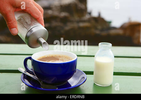 Tasse Kaffee auf einer Holzbank außerhalb, dass Zucker gegossen und eine kleine Flasche Milch daneben Stockfoto