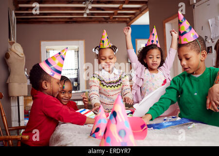 Kinder tragen Partyhüte und feiern am Tisch Stockfoto