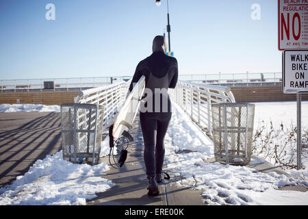 Schwarzer Teenager-Mädchen im Neoprenanzug tragen Surfbrett im winter Stockfoto