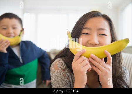 Asiatische Kinder halten Bananen vor Gesichtern für Lächeln Stockfoto