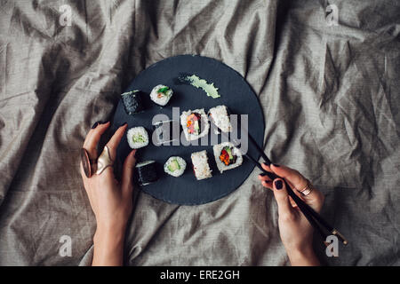 Hände der Frau erreichen für Teller Sushi auf Bett Stockfoto