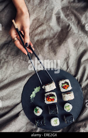 Hände der Frau erreichen für Teller Sushi auf Bett Stockfoto