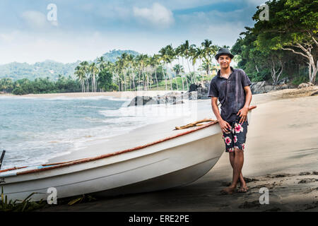 Hispanic Mann steht in der Nähe von Boot am Strand Stockfoto