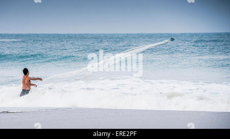 Mann beobachtet Boot in den Wellen des Ozeans vom Strand Stockfoto