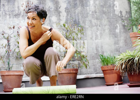 Ältere Frau kaukasischen aufrollen Yogamatte in Hof Stockfoto