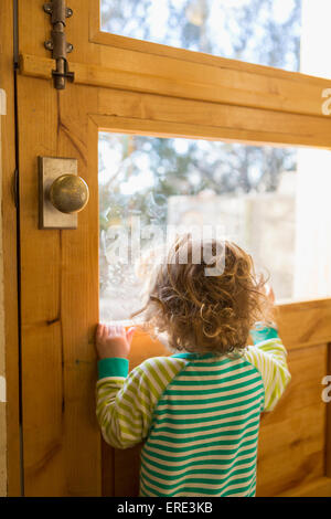 Kaukasische Junge schaut aus Türfenster Stockfoto