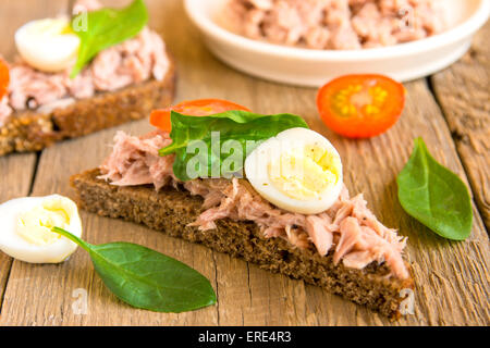 Frische hausgemachte Thunfisch-Sandwich mit Roggenbrot, Spinat, Wachteleiern und Tomaten auf hölzernen Hintergrund, horizontal, Nahaufnahme Stockfoto