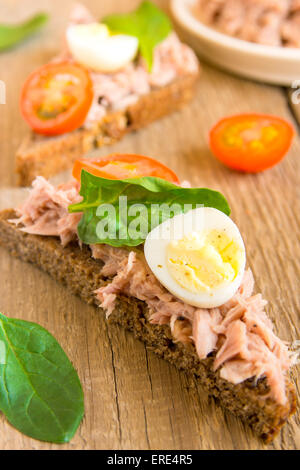 Frische hausgemachte Thunfisch-Sandwich mit Roggenbrot, Spinat, Wachteleiern und Tomaten auf hölzernen Hintergrund, vertikal, Nahaufnahme Stockfoto