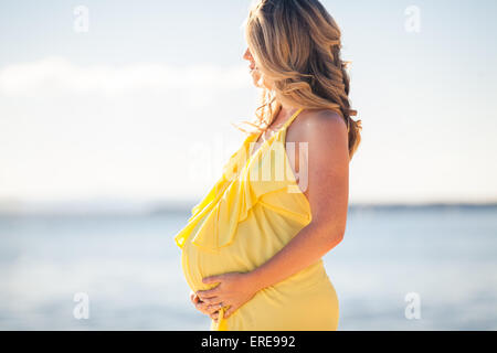 Höhenplan der schwangeren Frau mit langen Haaren im gelben Kleid am Strand Stockfoto