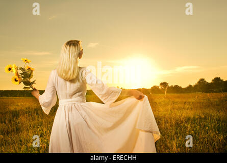 Schöne Frau mit Sonnenblumen im Feld bei Sonnenuntergang Stockfoto